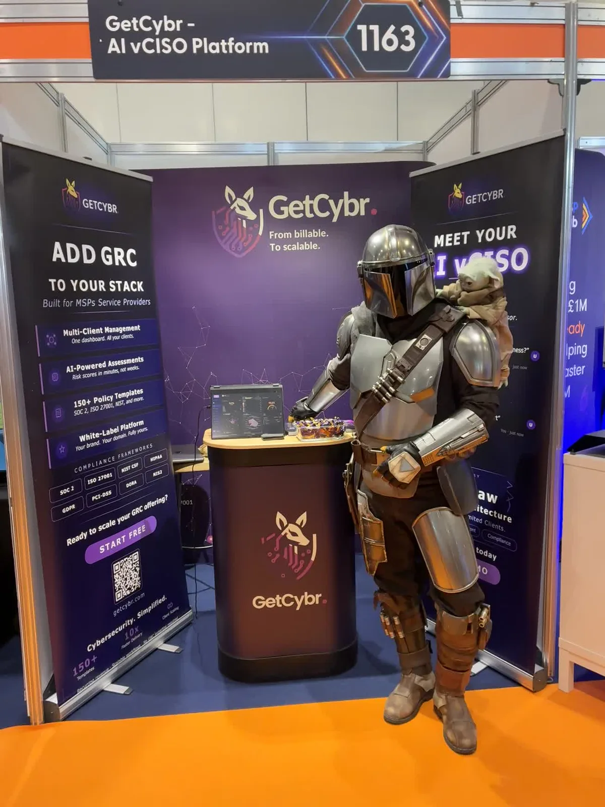 The GetCybr exhibition stand at MSP Show 2026, with overhead signage reading 'GetCybr – AI vCISO Platform' and the stand number 1163, roll-up banners covering multi-client management, AI-powered assessments, policy templates, and the white-label platform, a laptop showing the GetCybr dashboard, and a costumed Mandalorian character standing beside the podium.